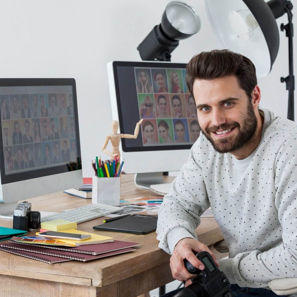 Happy Photographer Holding Camera At His Desk 9REYFMZ 1024x1024